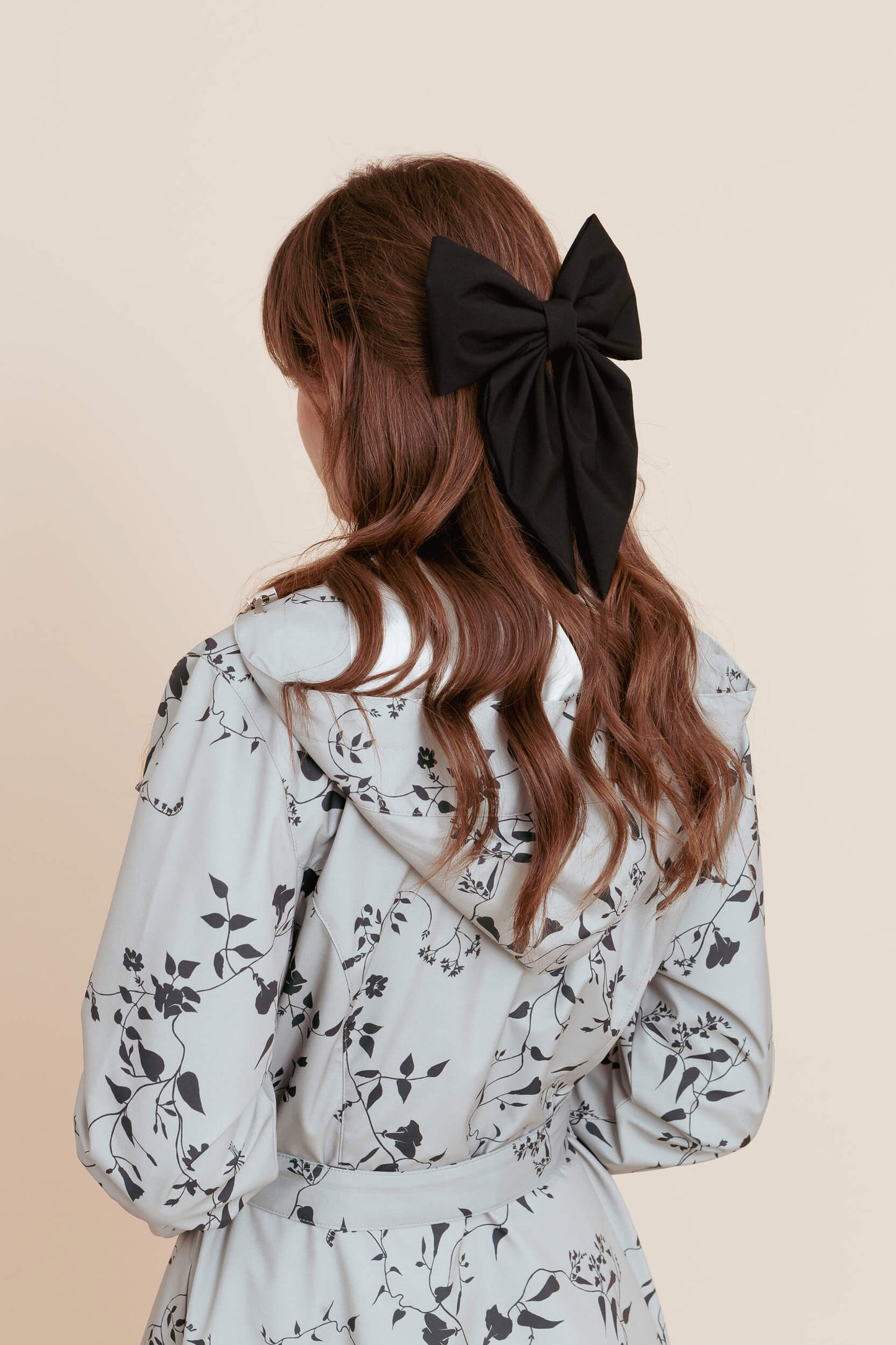 Model with long brown hair tied back with a black bow, wearing a minty color floral coat.