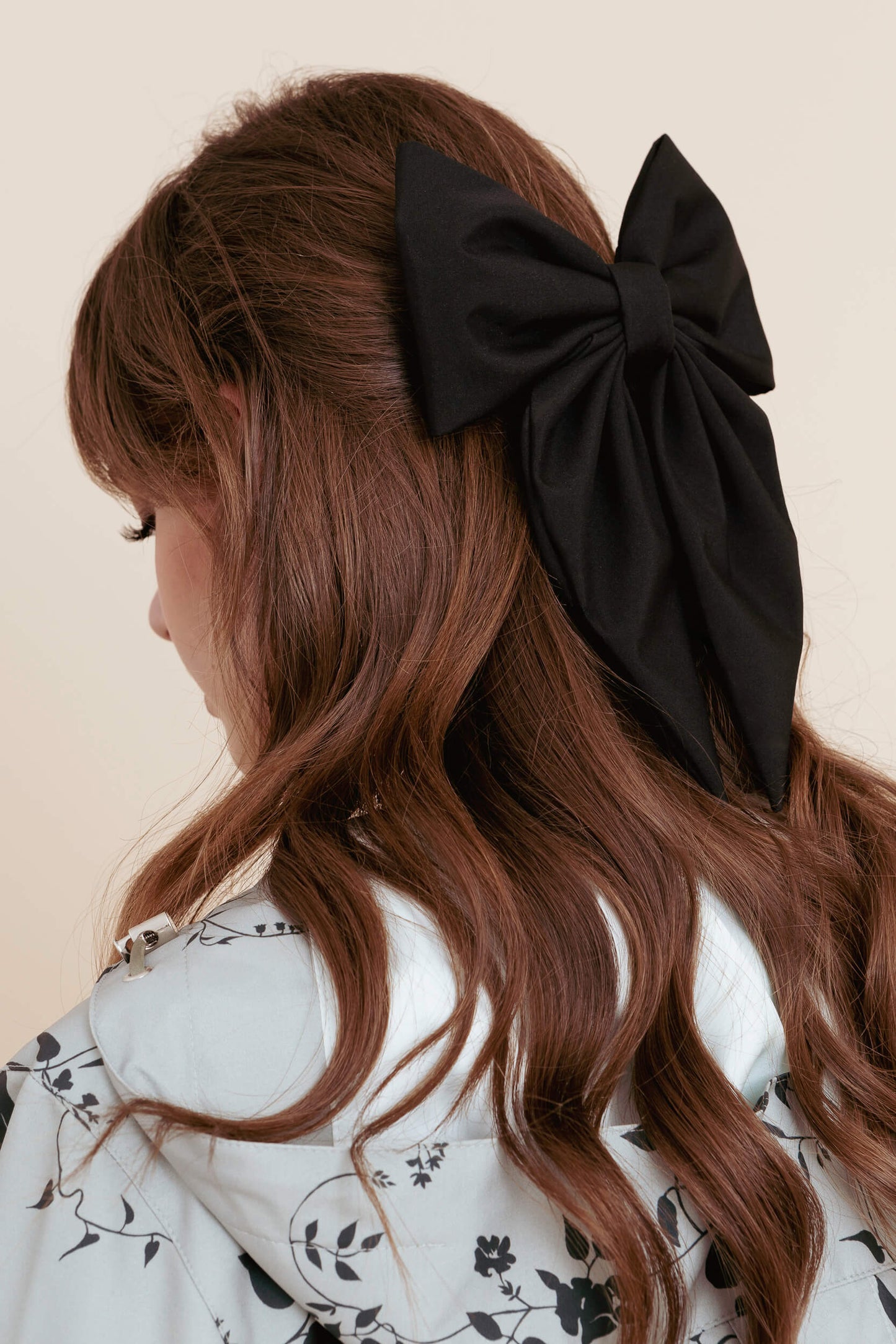 Woman with long wavy hair wearing a large black bow clip on a beige background
