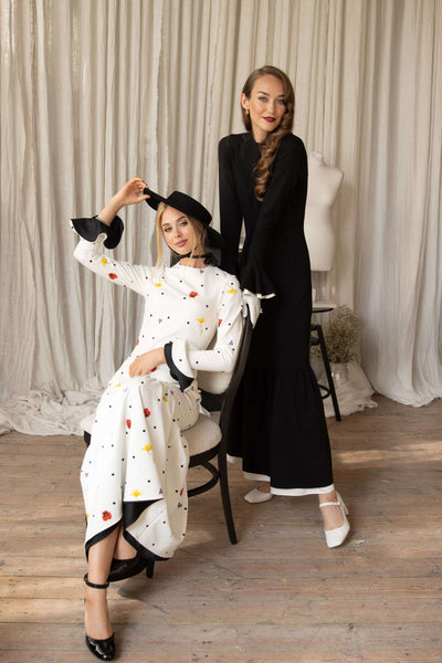 Two models wearing dancing romance and quiet elegance maxi dresses, posing in a stylish setting with a curtains in the background.