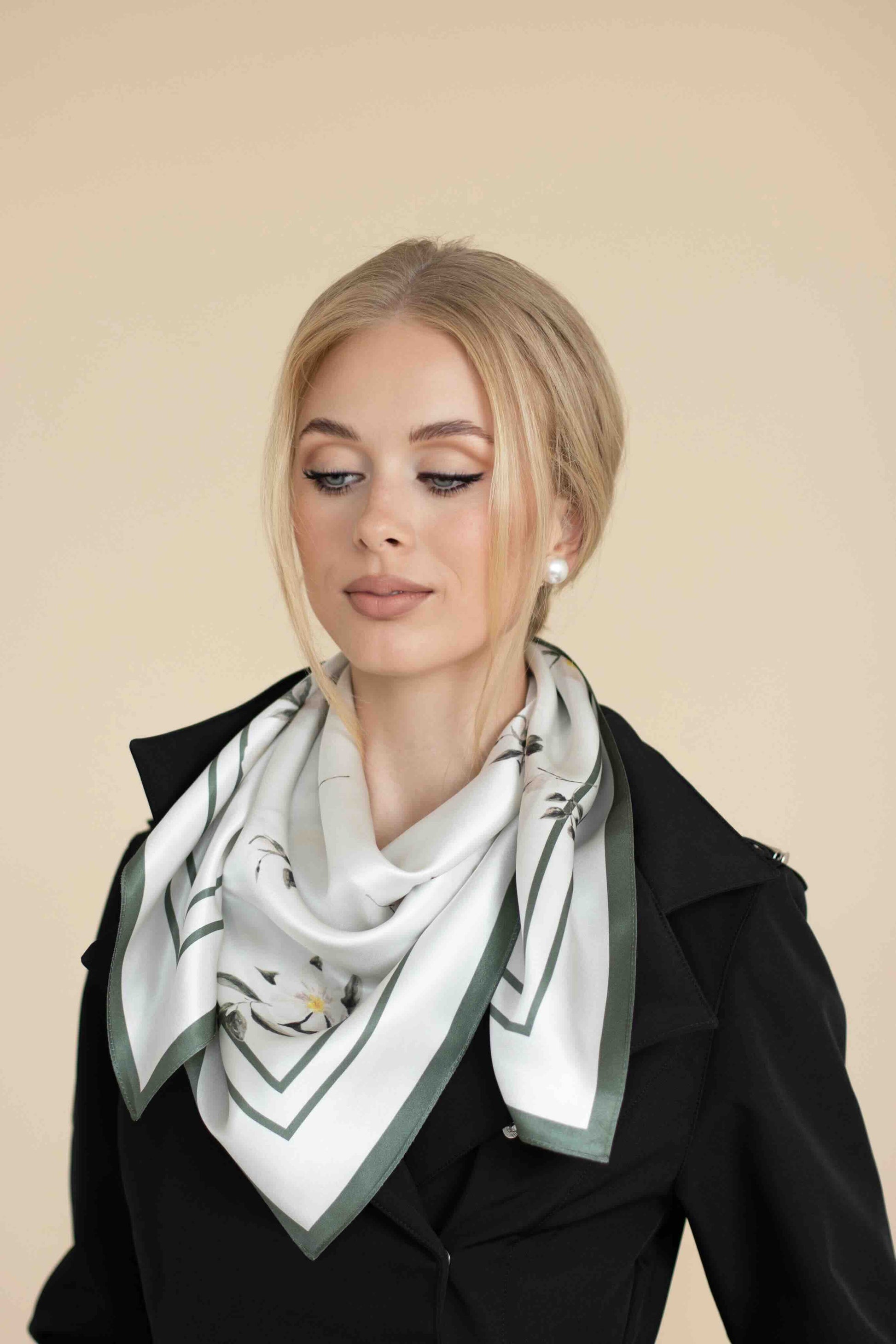 Woman wearing a black coat and a white scarf with green accents on a beige background