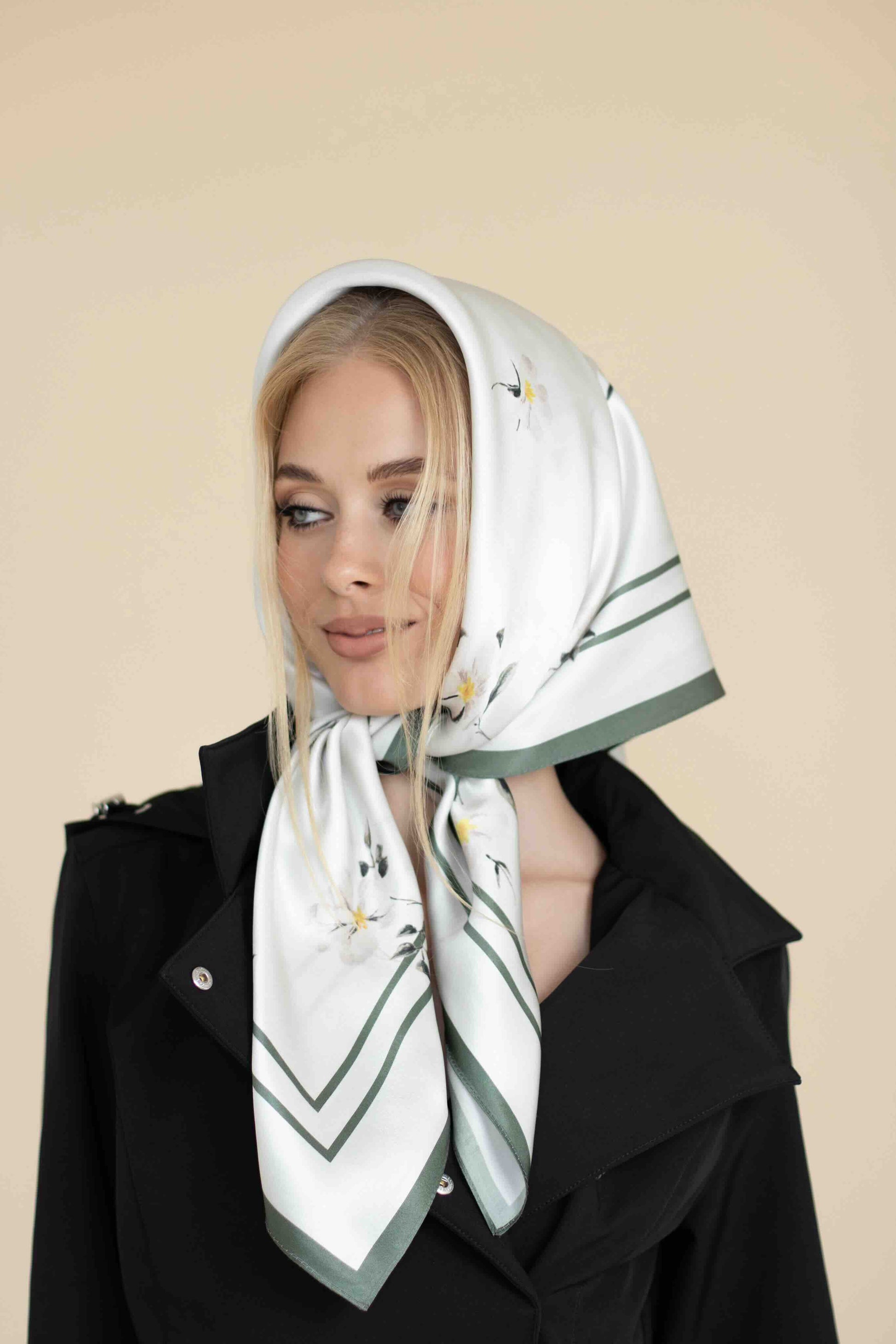 Woman wearing a white scarf with green accents and floral patterns on a beige background