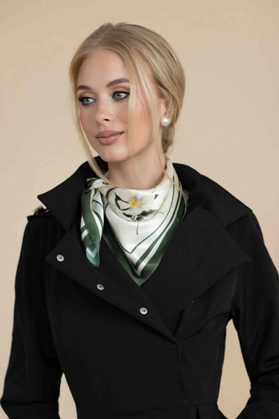 Woman wearing a black coat with a green and white patterned scarf against a beige background