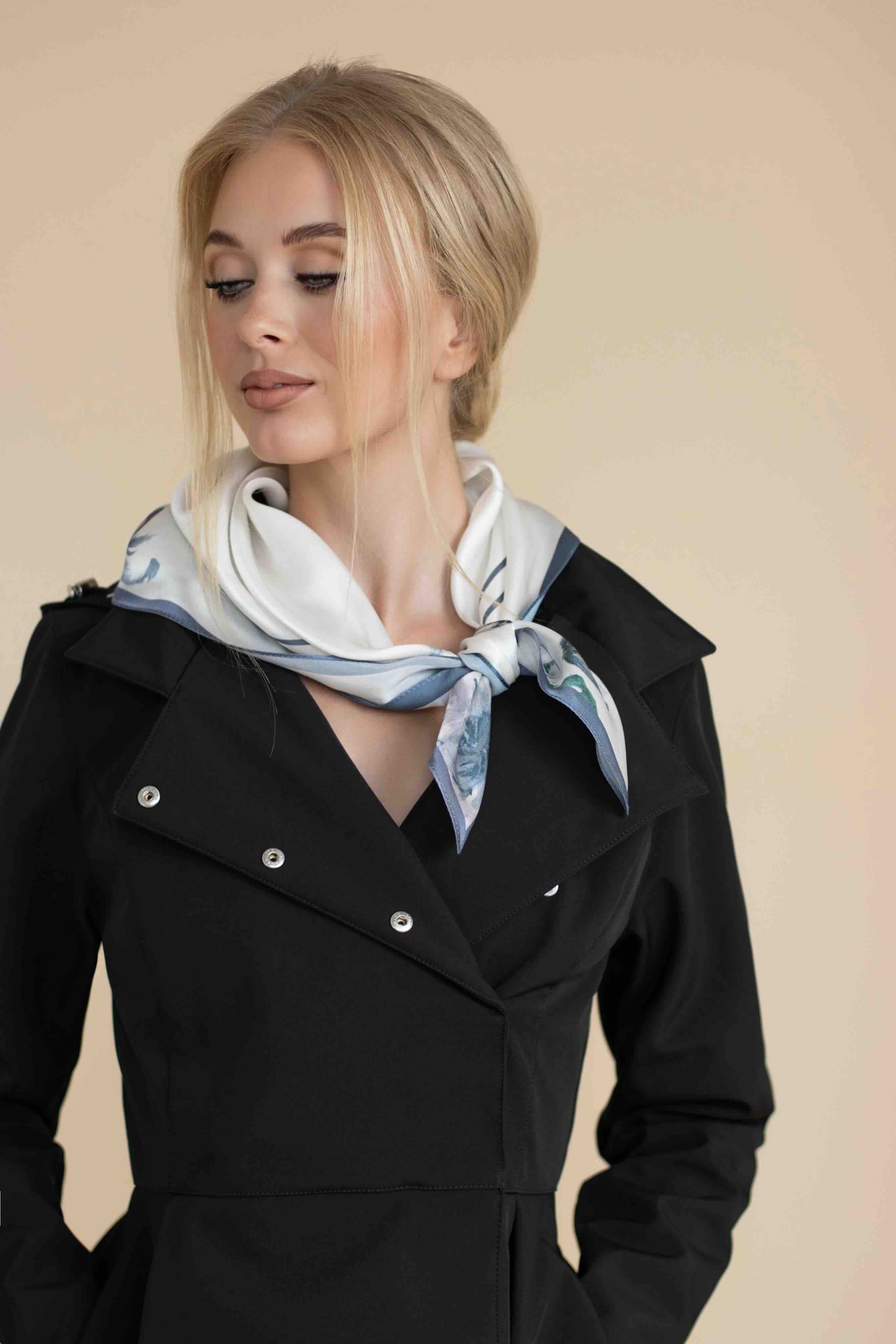 Woman wearing a black coat and a patterned scarf against a beige background