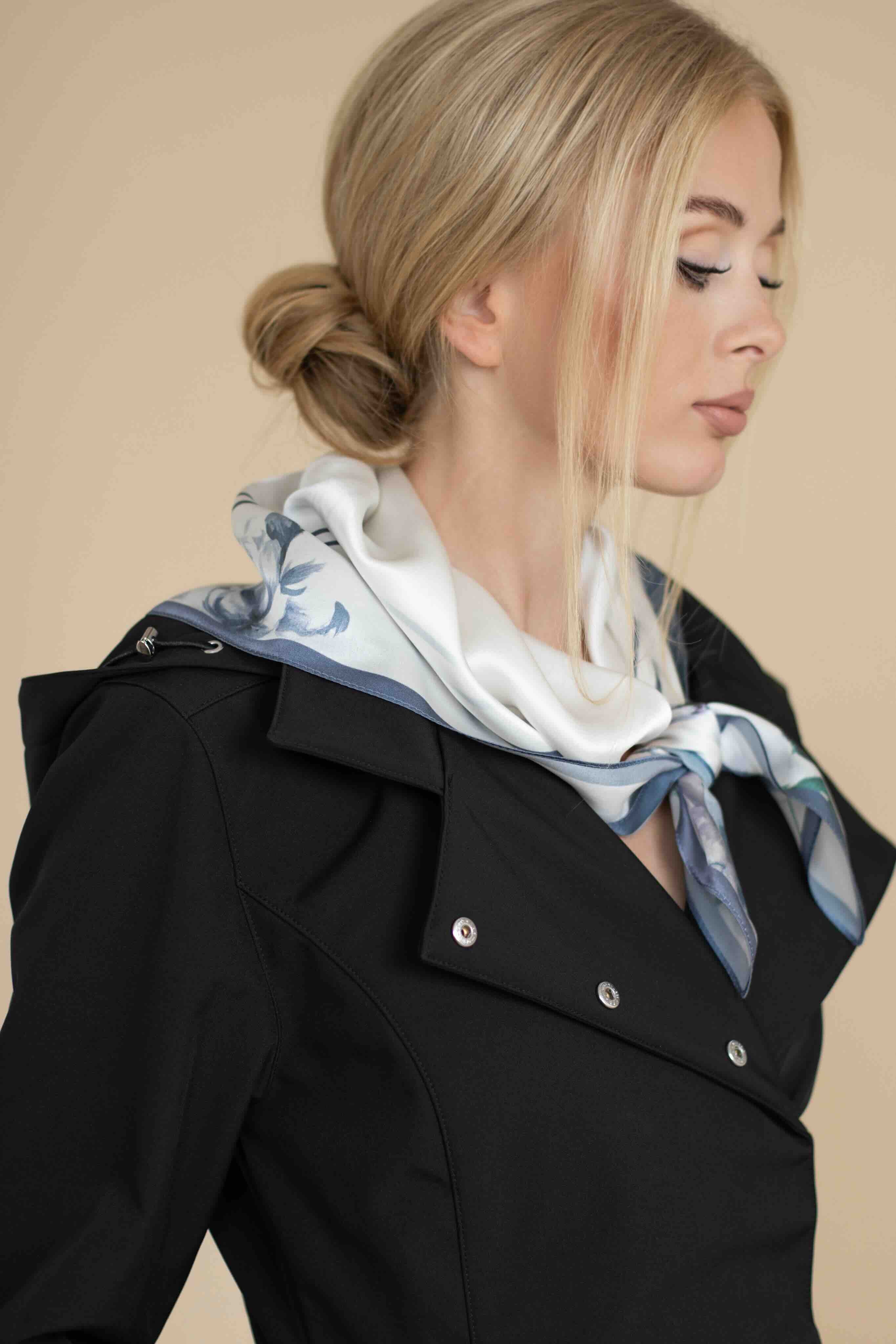 Woman wearing a black coat with a patterned scarf on a beige background