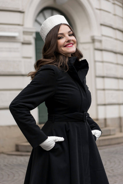 Model in a black winter coat with flared skirt and detachable hood, elegant and versatile design.