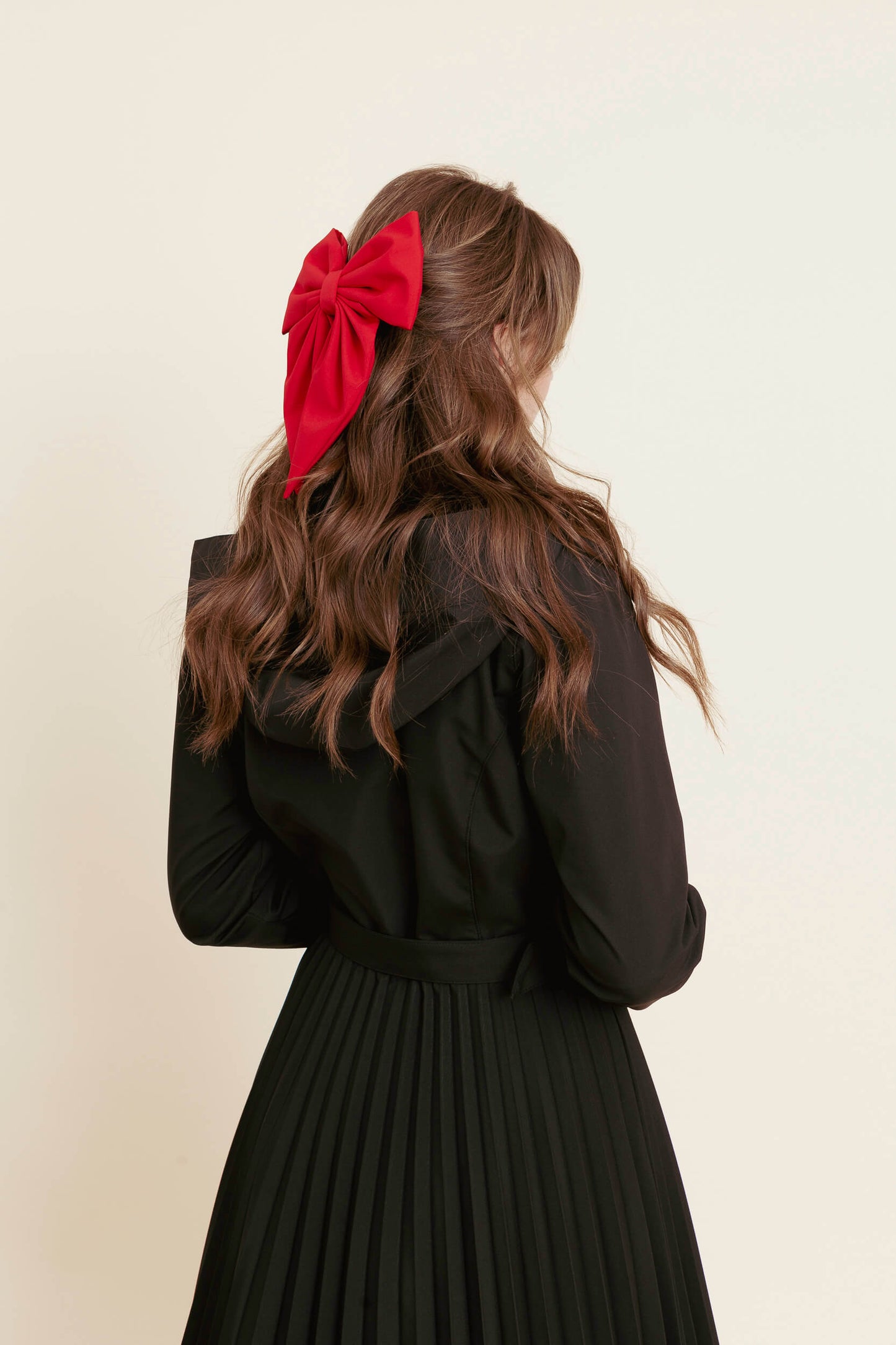 model wearing a black coat with a red bow in her hair against a beige background