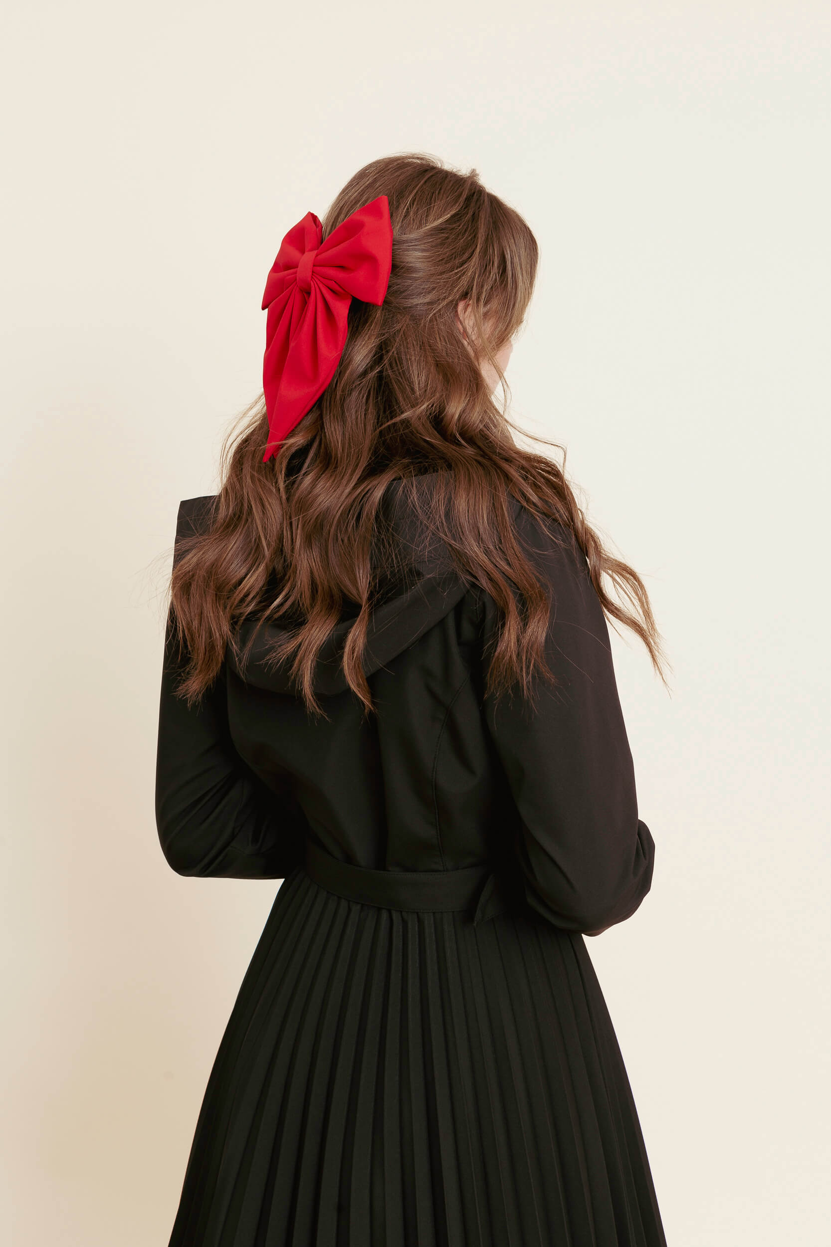 model wearing a black coat with a red bow in her hair against a beige background