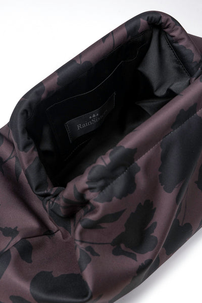 Close-up of a Rainsisters clutch bag with a dark floral pattern in brown with black floral print, showing the black interior lining and a brand label.
