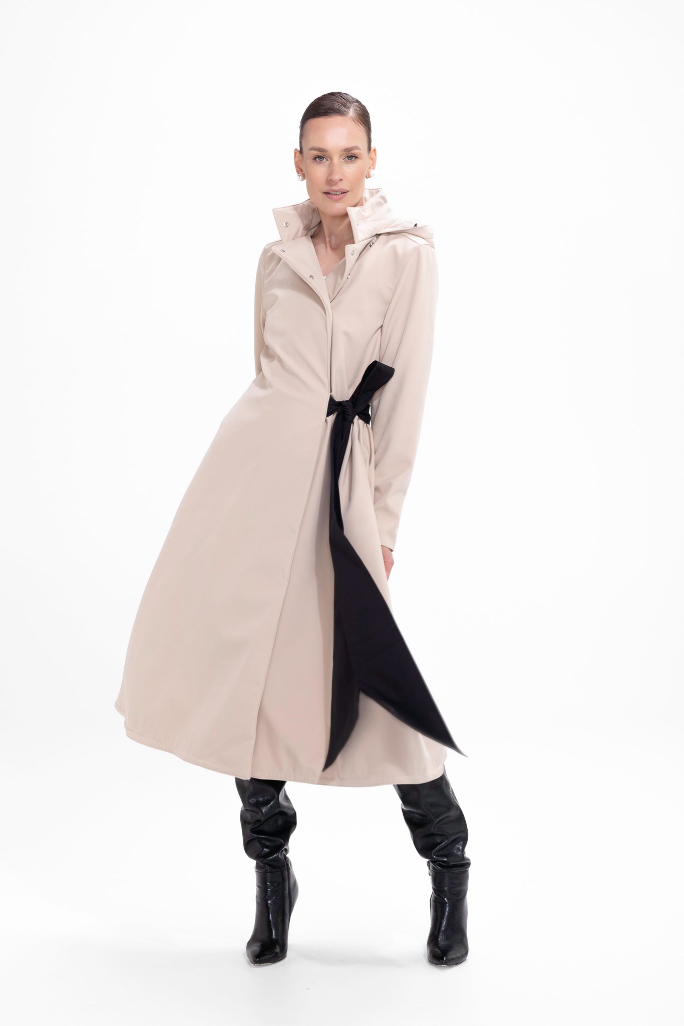 Model in motion wearing elegant beige A-line trench coat with feminine bow waist detail