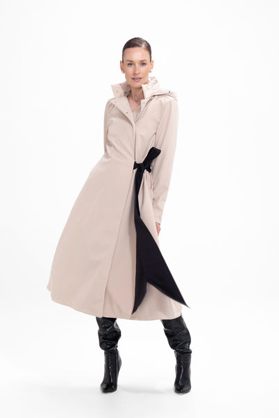 Model in motion wearing elegant beige A-line trench coat with feminine bow waist detail