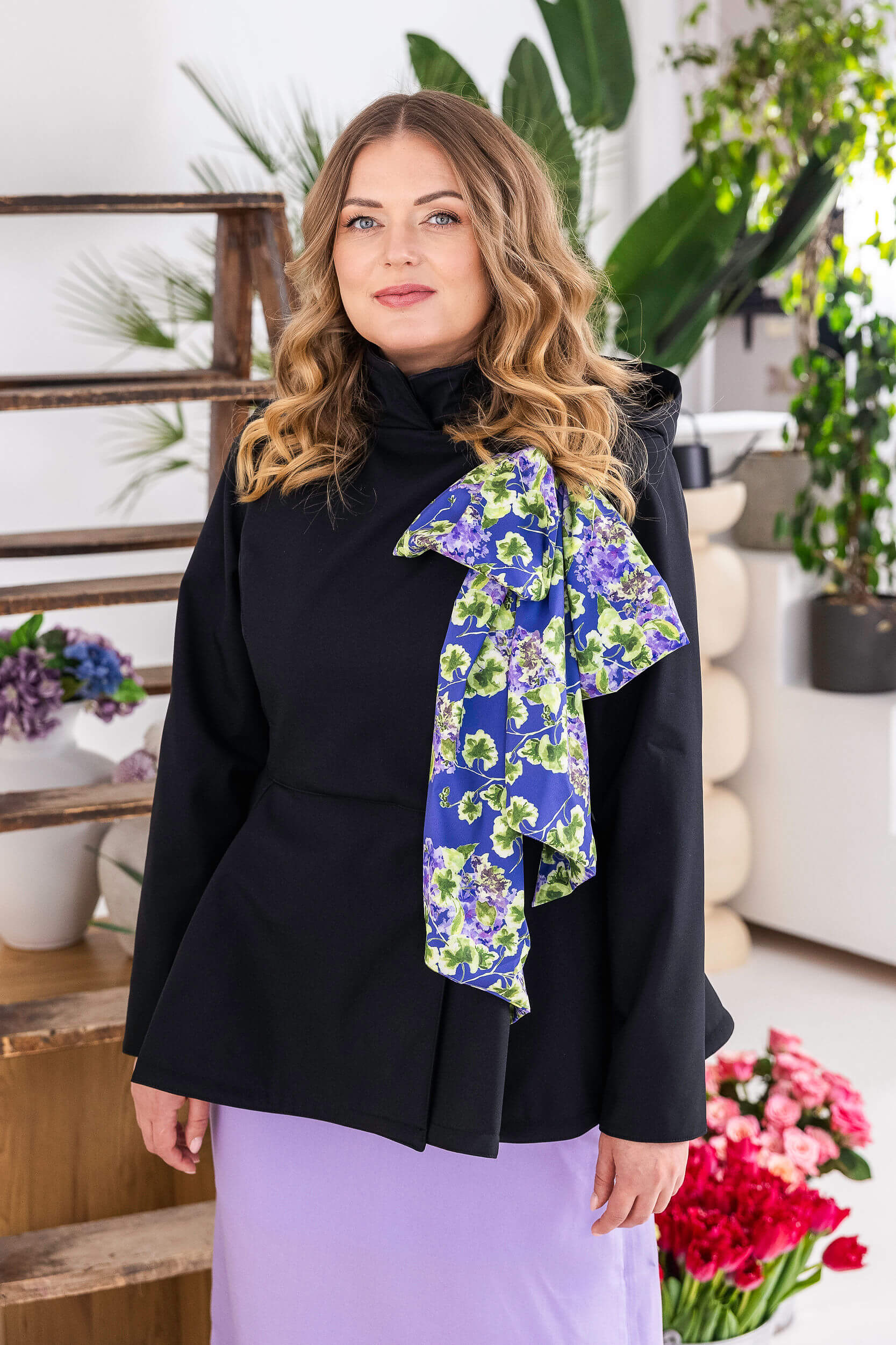 Women’s black double-breasted waterproof jacket with removable violet floral scarf and flowing silhouette.