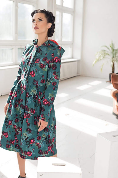 Model in motion wearing elegant green floral women's coat with flowing pleated silhouette