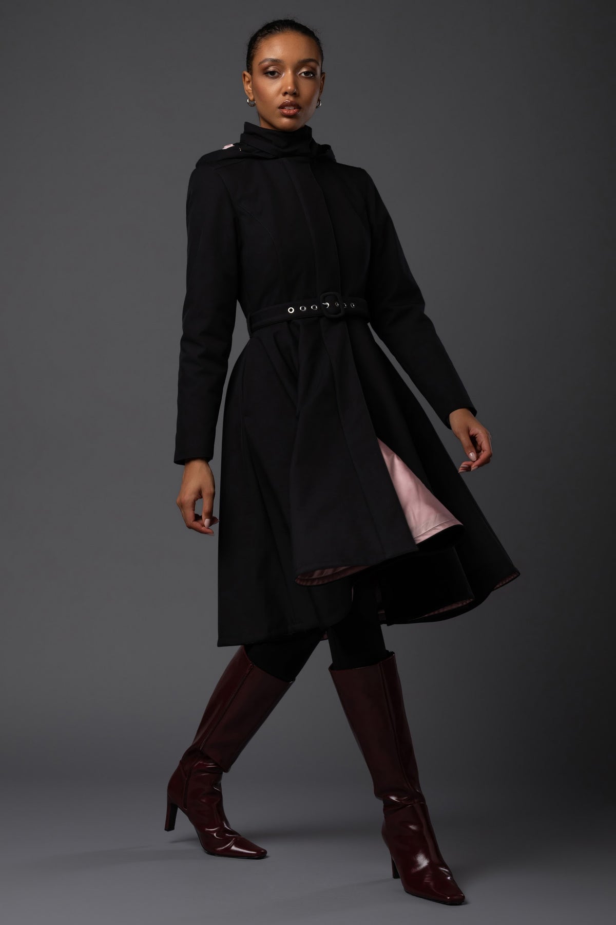 A model wears a feminine black waterproof winter coat with a fitted bodice and flowing full-circle skirt designed by Rainsisters.
