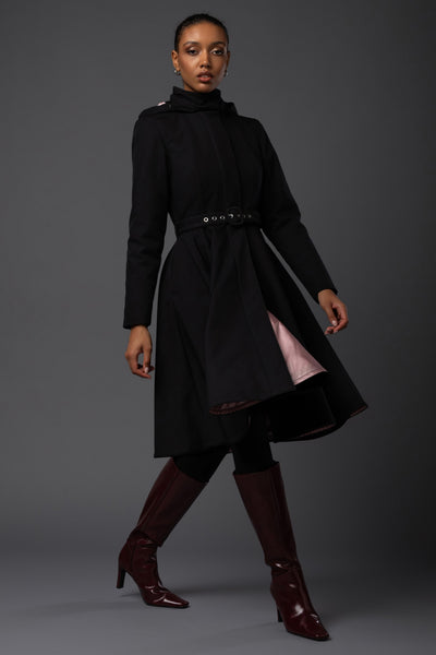 A model wears a feminine black waterproof winter coat with a fitted bodice and flowing full-circle skirt designed by Rainsisters.