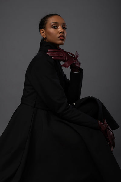 A model wears an elegant black waterproof winter coat with a fitted waist and full-circle skirt by Rainsisters.