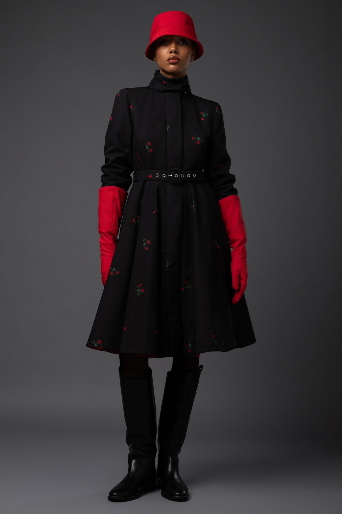 A model showcases a feminine black waterproof winter coat with delicate red strawberries, fitted waist and bold red lining by Rainsisters.