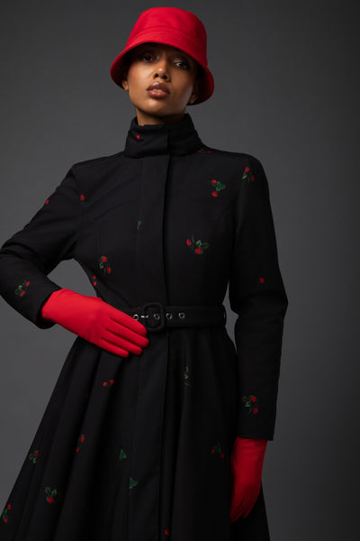 A model showcases an elegant black winter coat with delicate red strawberry pattern and contrasting red lining by Rainsisters.