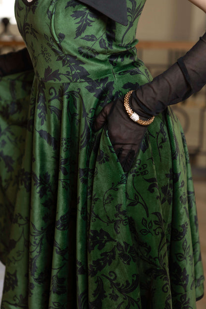 Forest Kiss full-circle velvet dress in green, featuring black floral print, side pockets, and elegant adjustable straps.