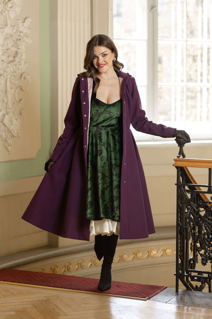 Elegant green velvet dress with black graphic florals, flowing full-circle skirt, hidden pockets, and bow-tied shoulder straps.