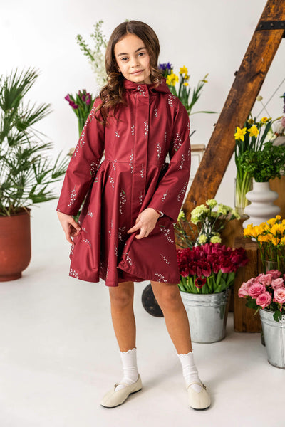 Young girl wearing a red raincoat with floral pattern in a room.