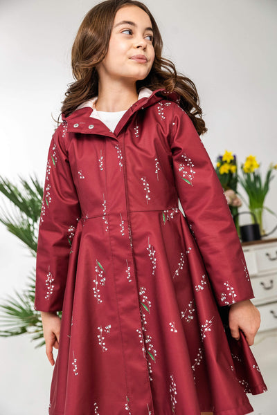 Girl wearing a red floral-patterned raincoat indoors.