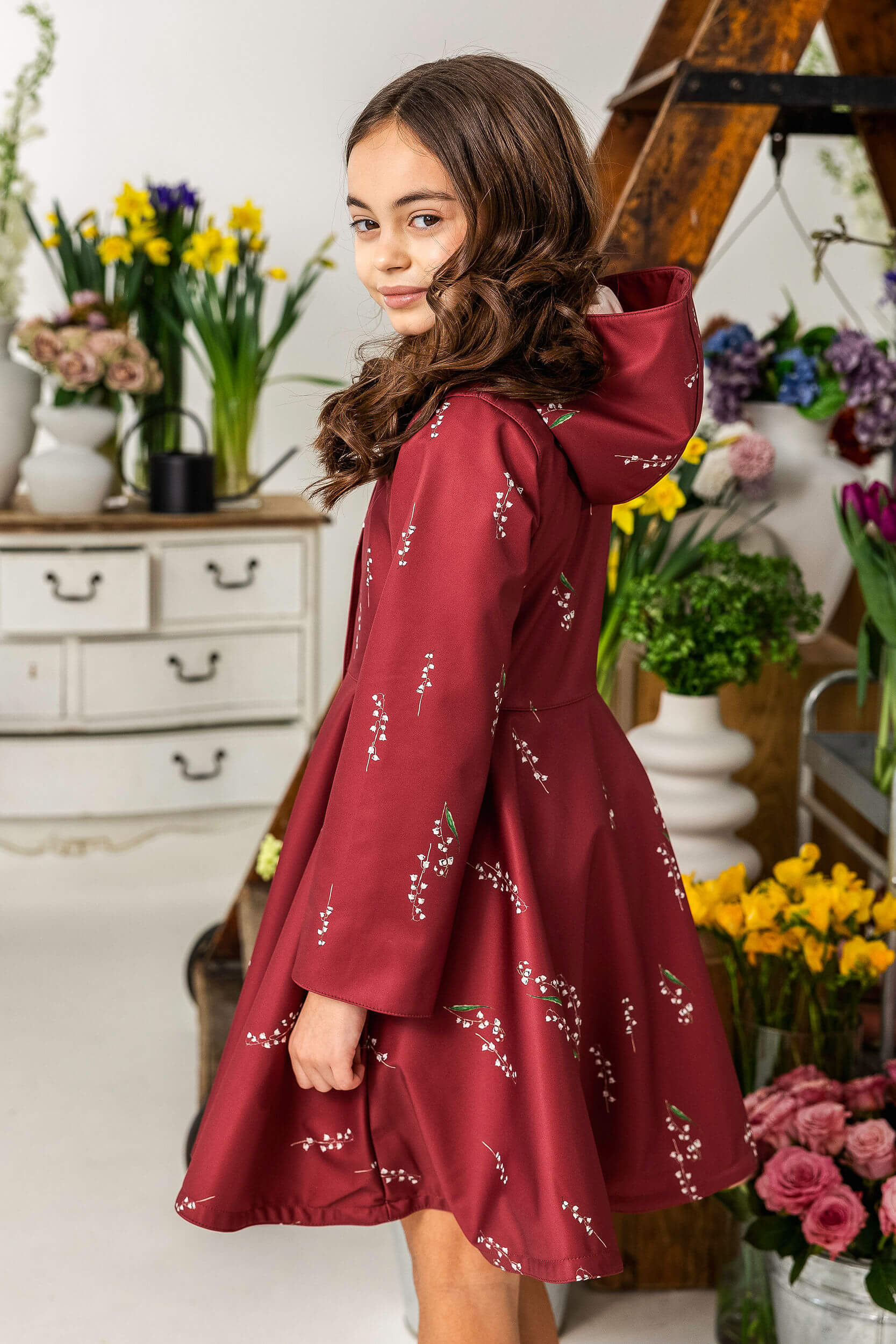 Girl in a burgundy coat with floral patterns standing in a room with flowers