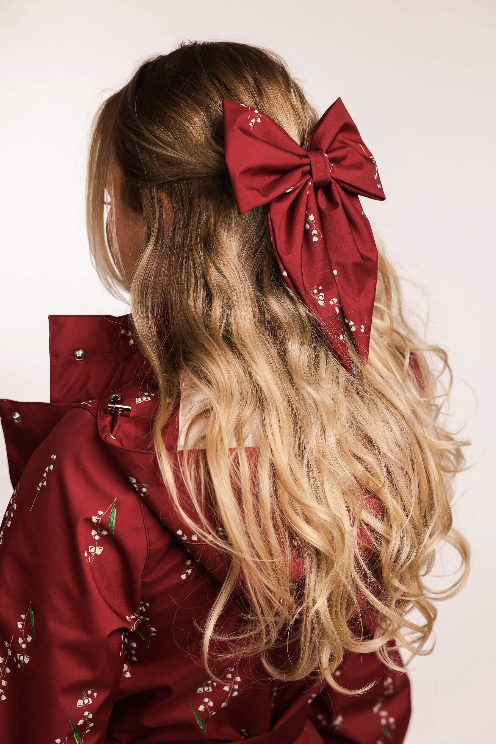 Person with long blonde hair wearing a large red bow, wearing a red floral outfit.