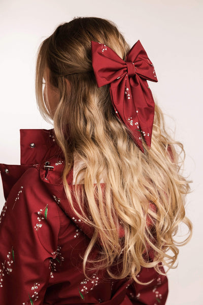 Person with long blonde hair wearing a large red bow, wearing a red floral outfit.