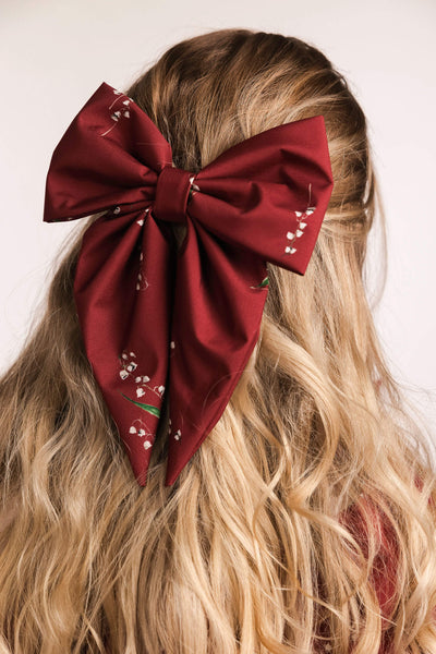 Red bow with floral details in blonde hair against a neutral background