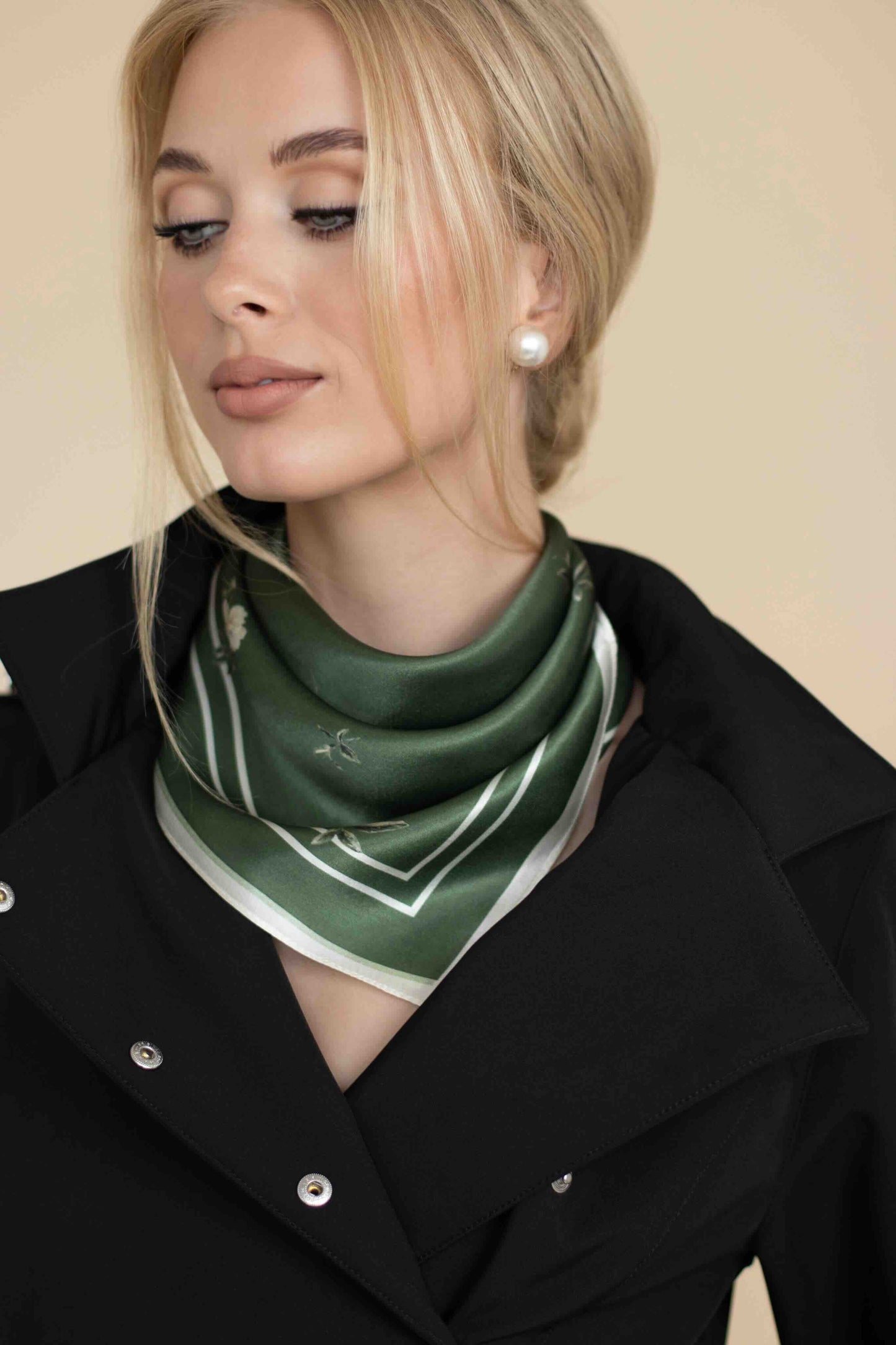 Woman wearing a green scarf with a black coat against a beige background