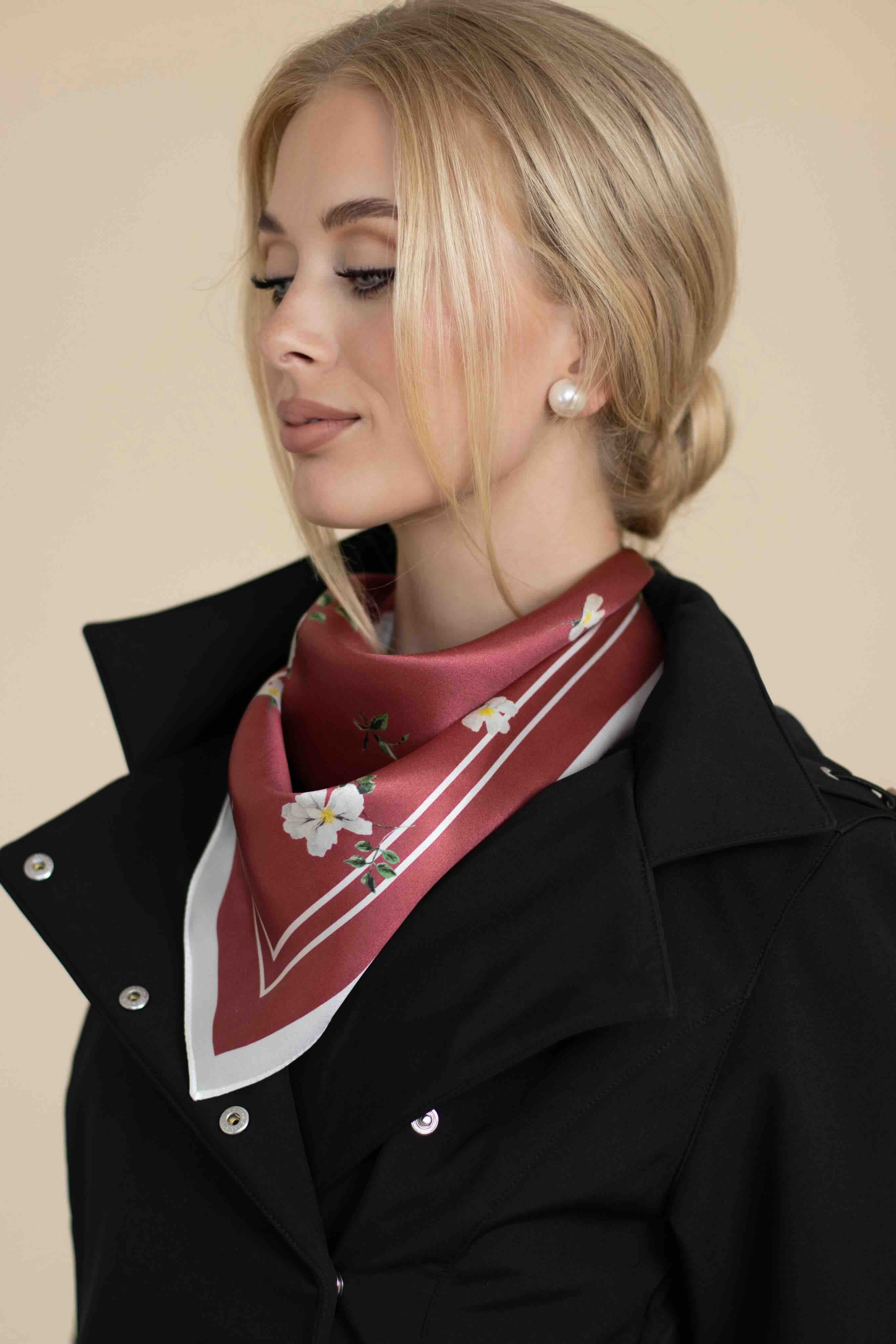 Woman wearing a red scarf with white patterns and a black coat against a beige background