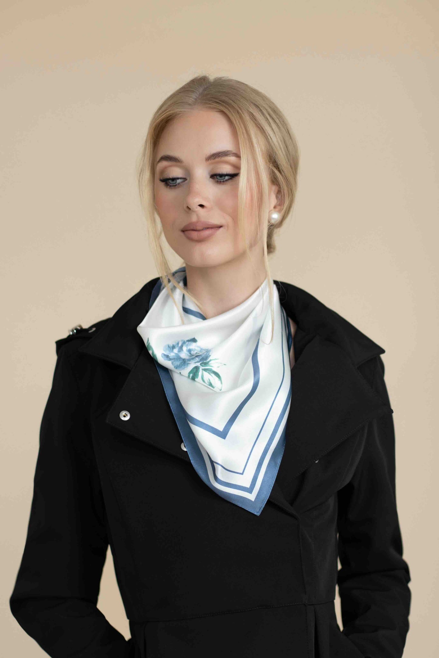 Woman wearing a black coat with a white scarf featuring blue floral pattern on a beige background