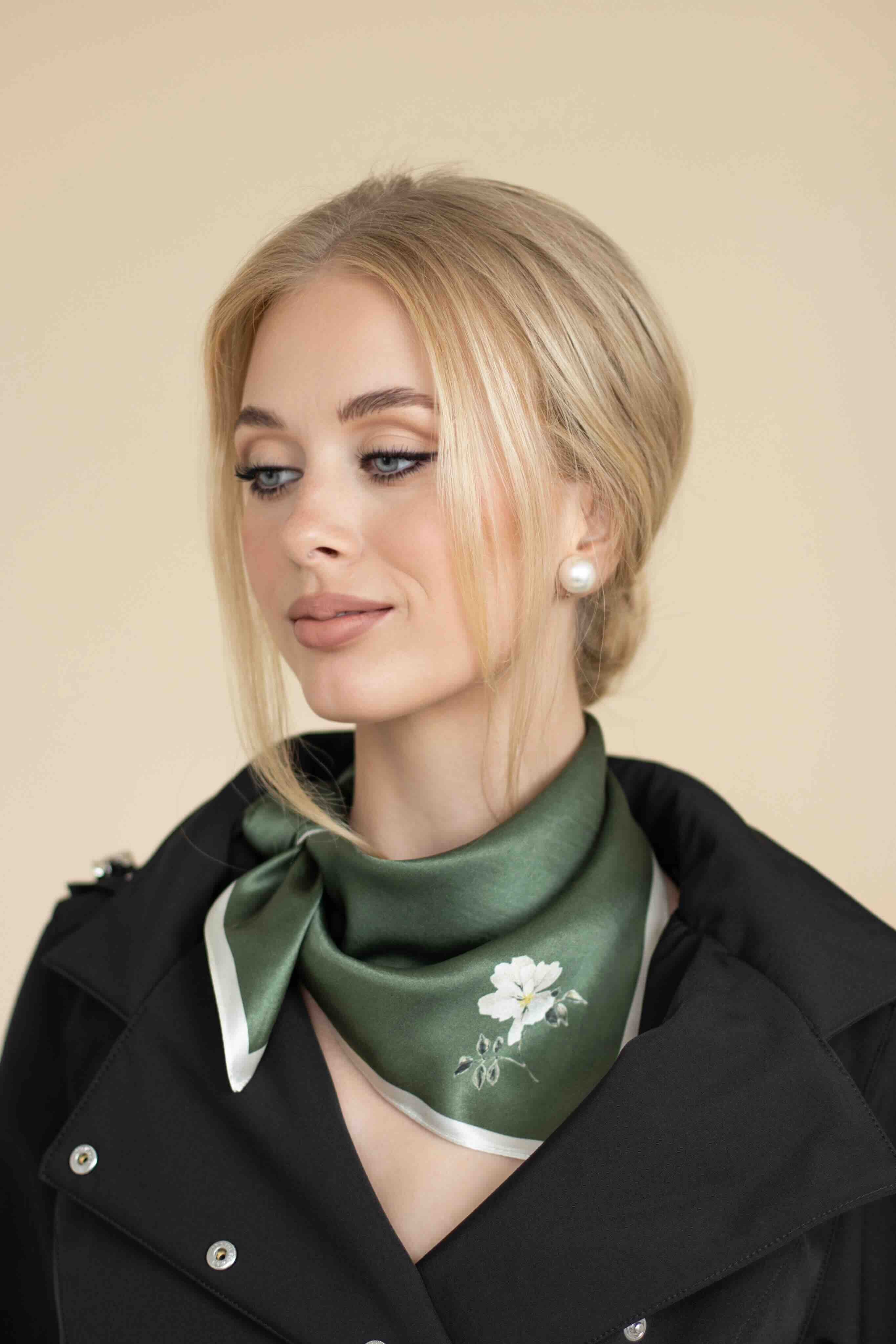 Woman wearing a green scarf with a floral design, standing against a beige background.