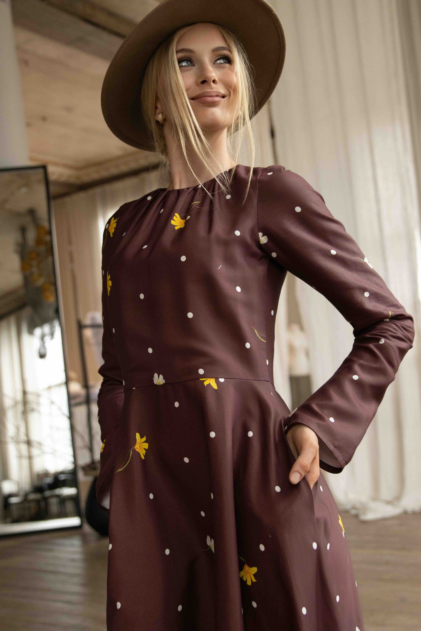 Romantic brown midi dress with floral and polka dot pattern, softly gathered neckline, and long flared sleeves.