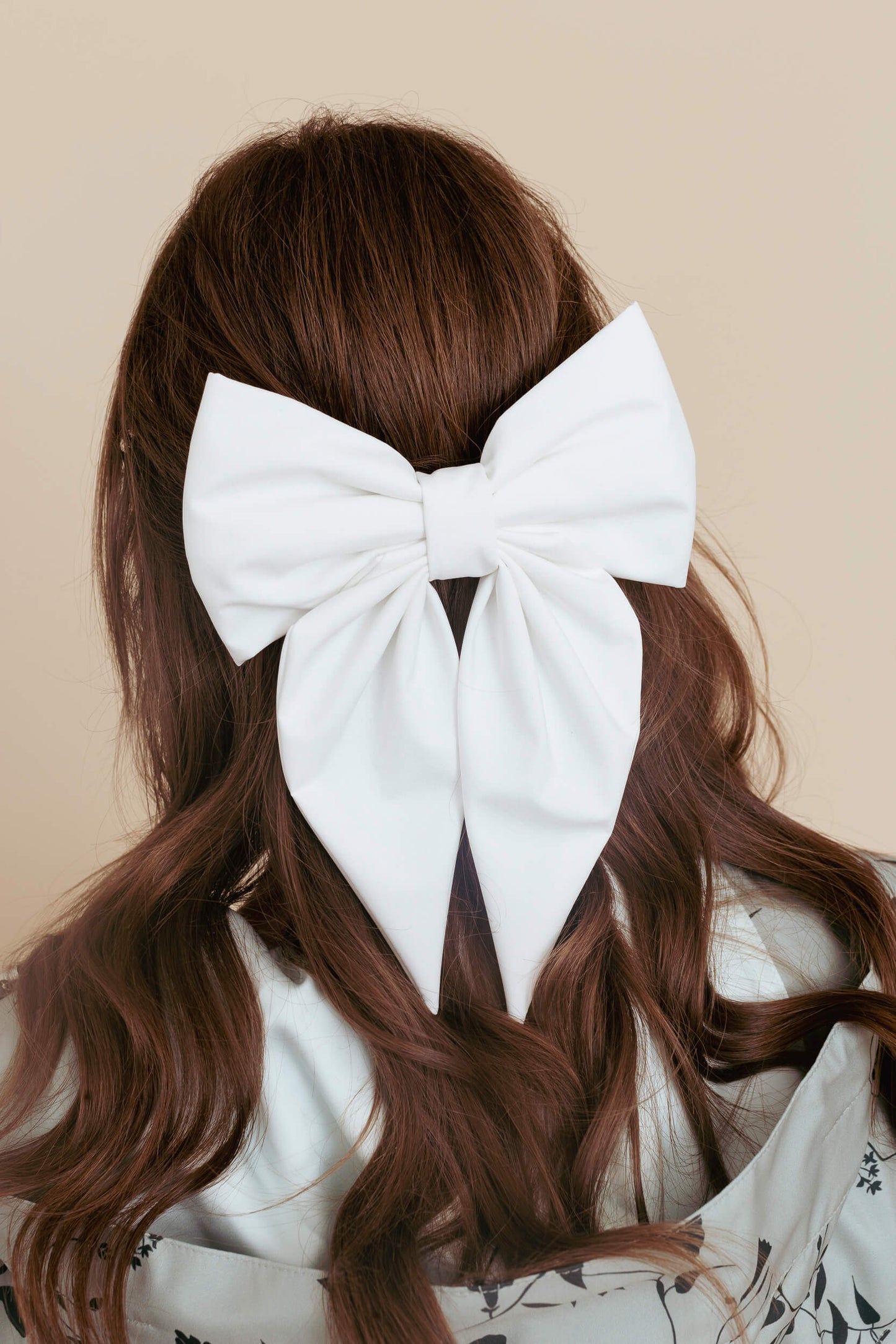 White bow in brown hair against a beige background