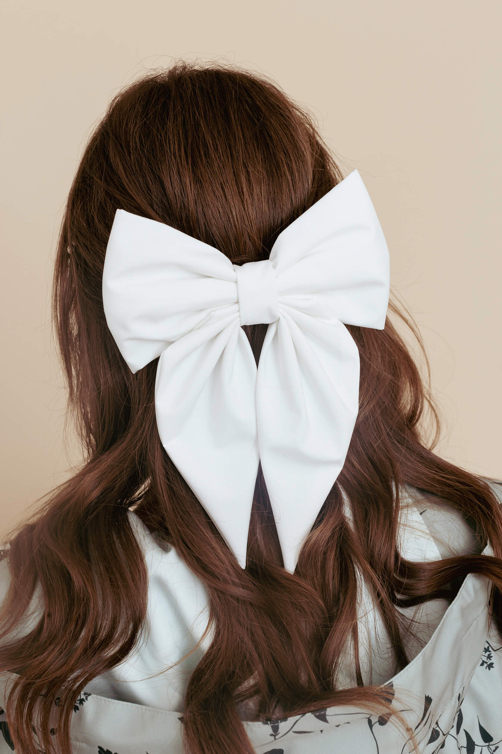 White bow in brown hair against a beige background