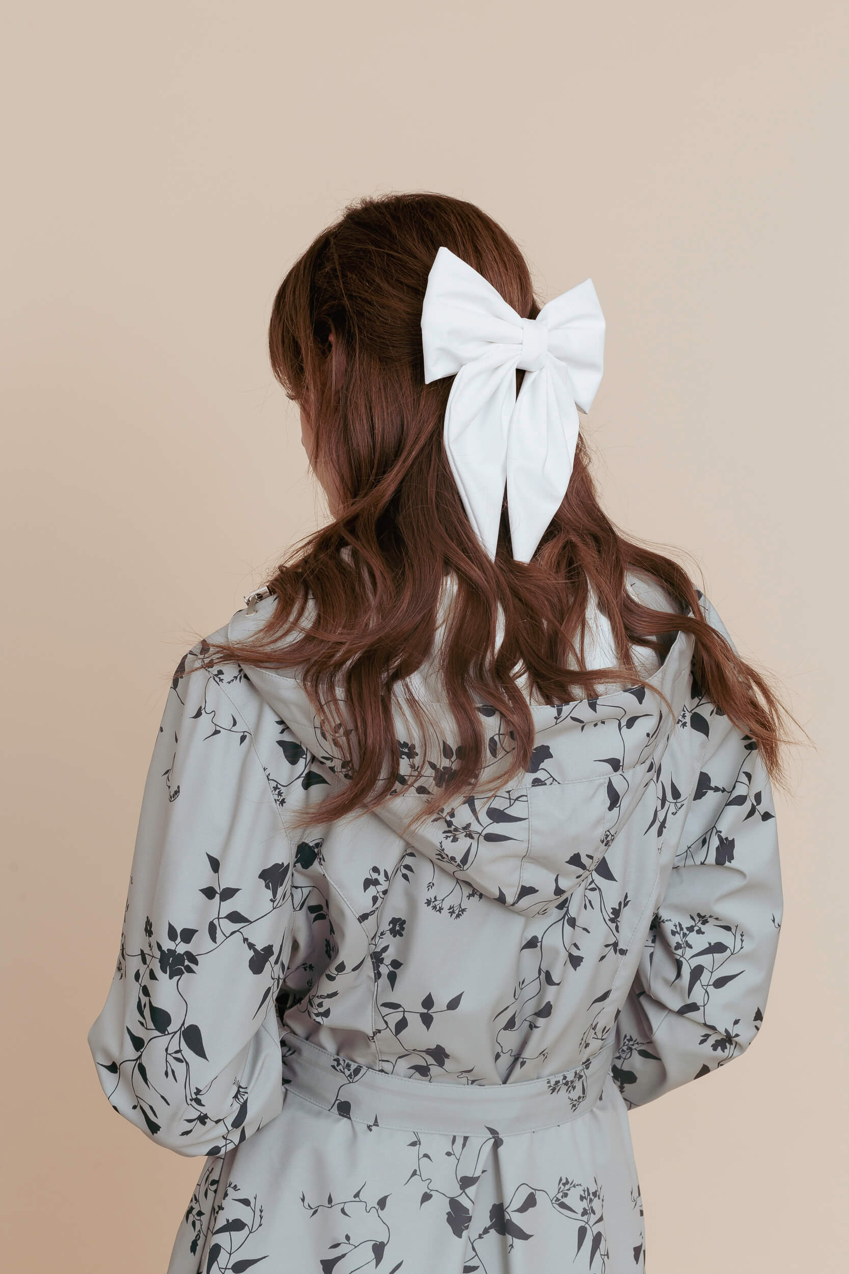 Model wearing a floral minty color coat with a white bow in her hair on a beige background