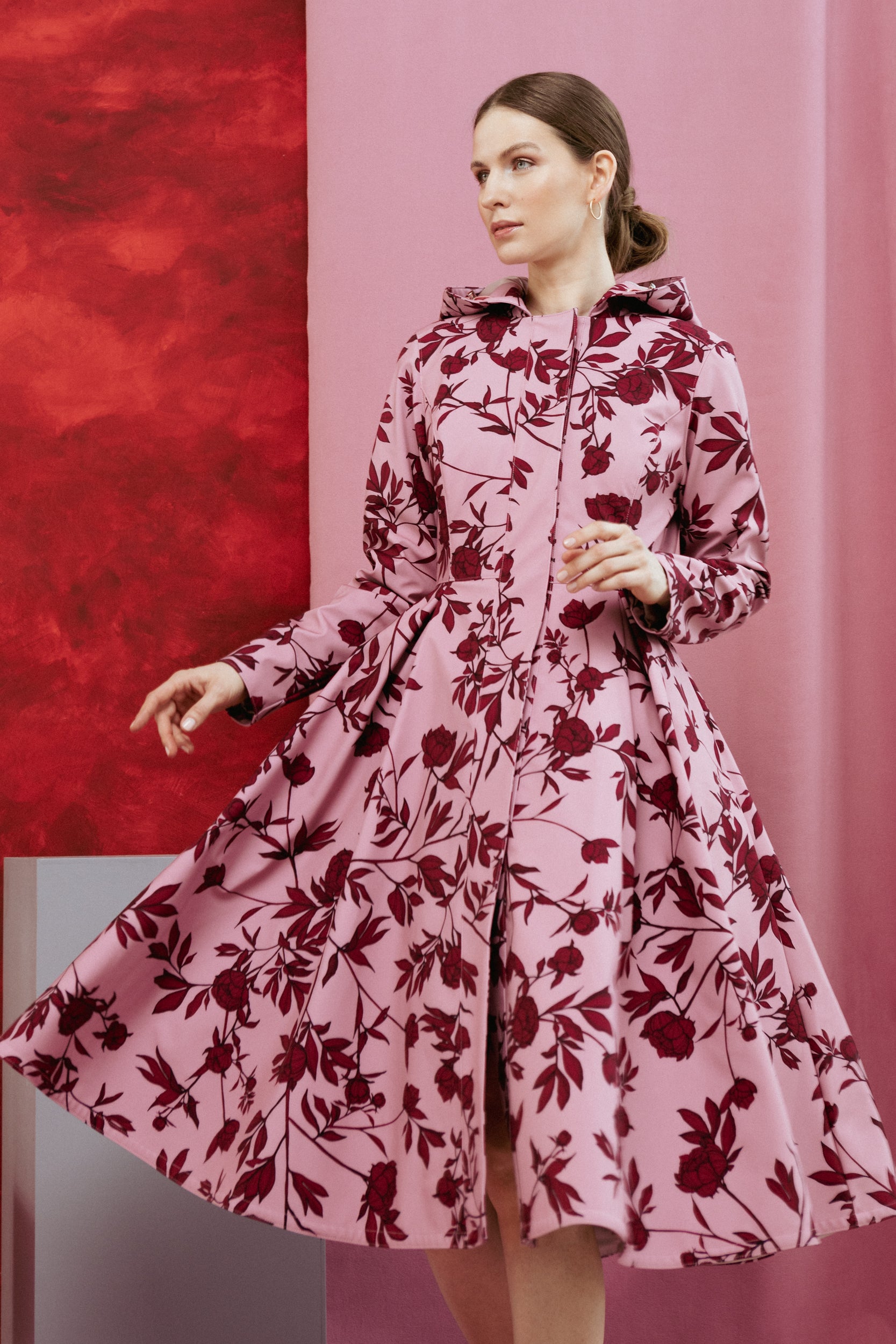 Model wearing the Peony Bloom coat, showcasing the fitted upper body and flared vintage pleated skirt in gentle pink with bold burgundy peony print.